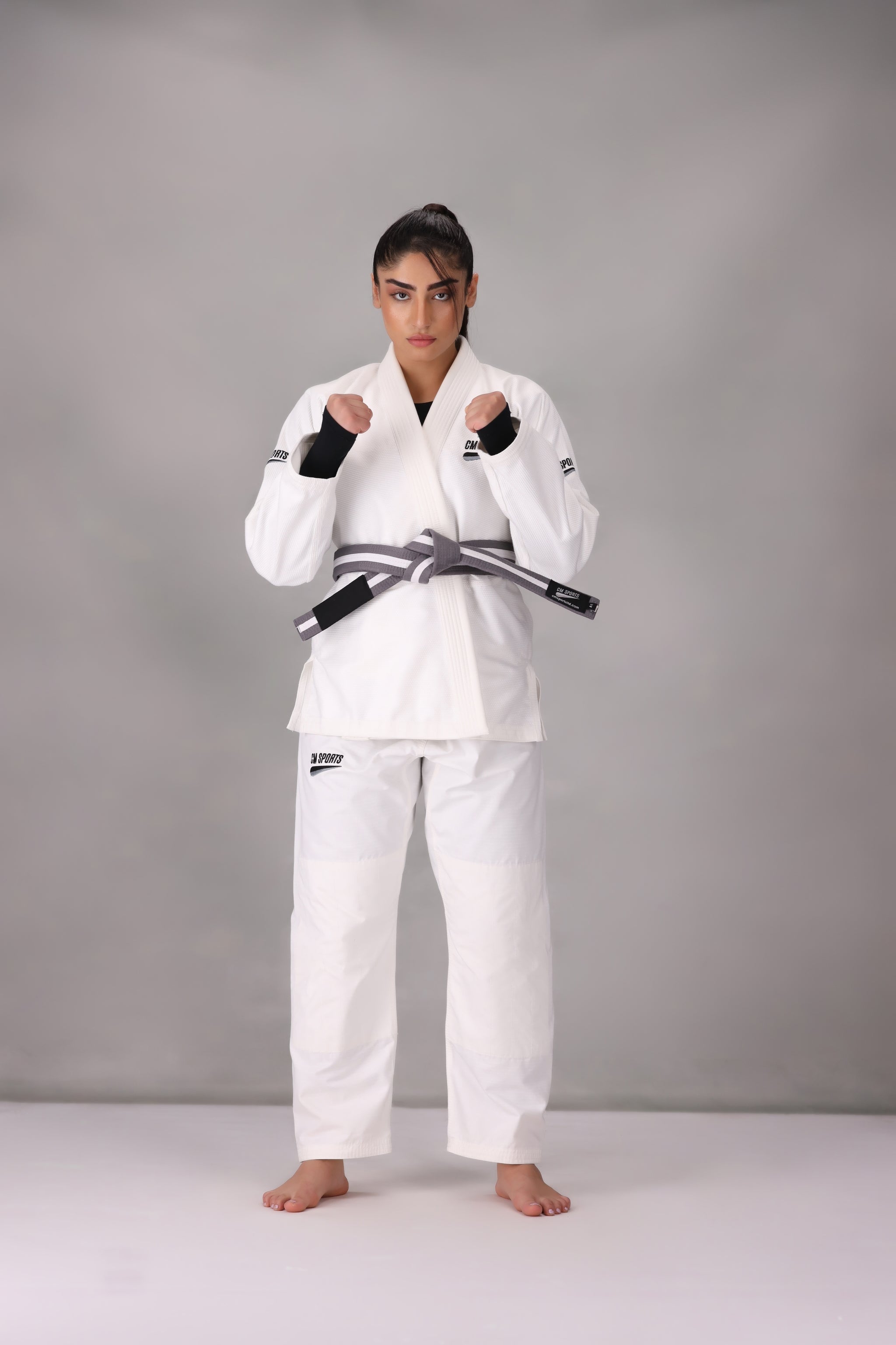 Woman wearing a custom white BJJ Gi with a black belt, standing on a gray background UK Brazilian Jiu Jitsu uniform
