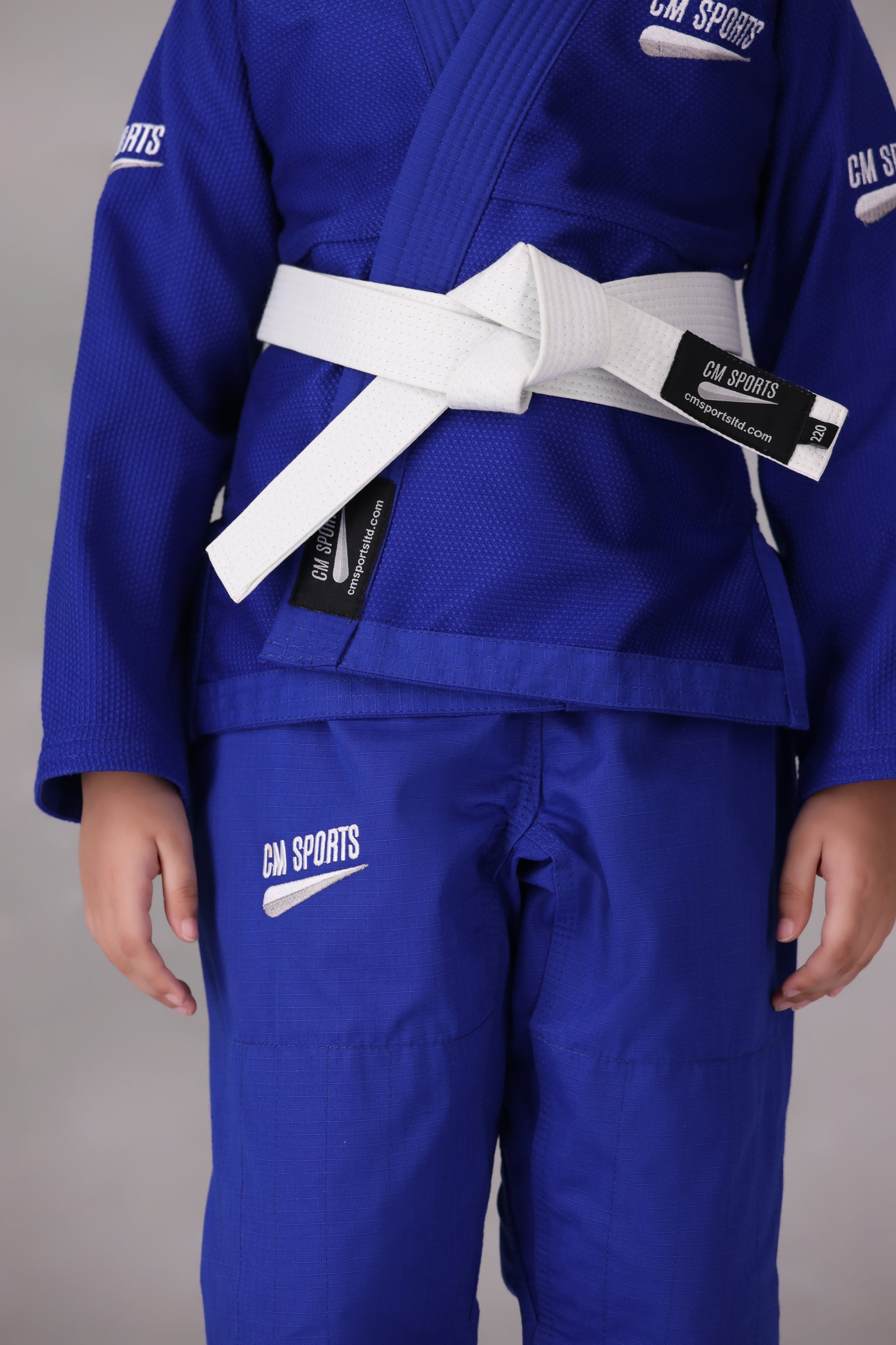 Child wearing a custom kids Jiu Jitsu Gi in the UK, blue Brazilian Jiu Jitsu uniform with a white belt on a gray background