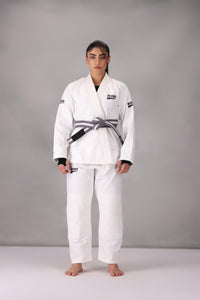 Woman wearing a custom white BJJ Gi with a black belt, standing on a gray background UK Brazilian Jiu Jitsu uniform
