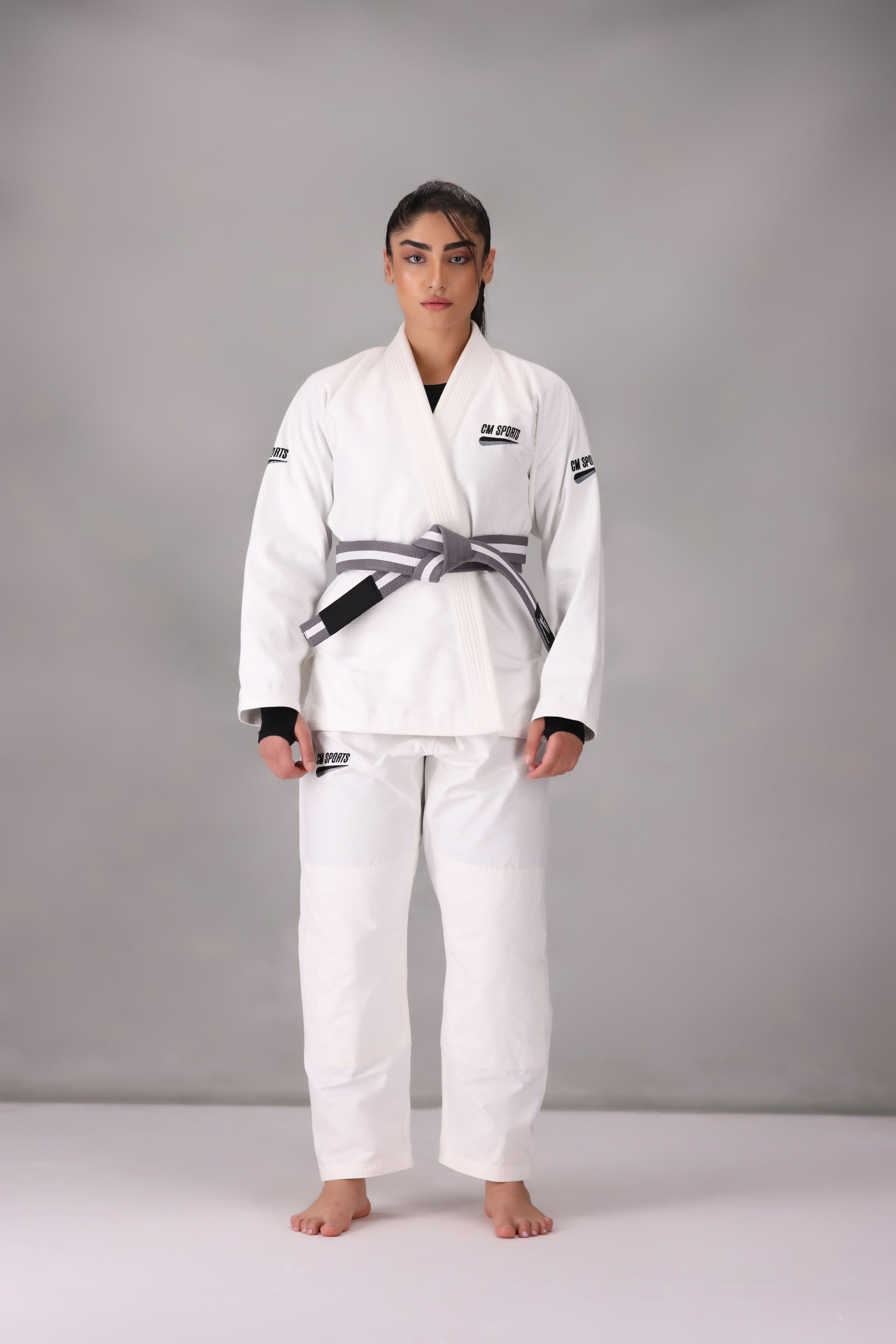 Woman wearing a custom white BJJ Gi with a black belt, standing on a gray background UK Brazilian Jiu Jitsu uniform