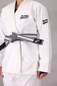 Woman wearing a custom white BJJ Gi with a black belt, standing on a gray background UK Brazilian Jiu Jitsu uniform