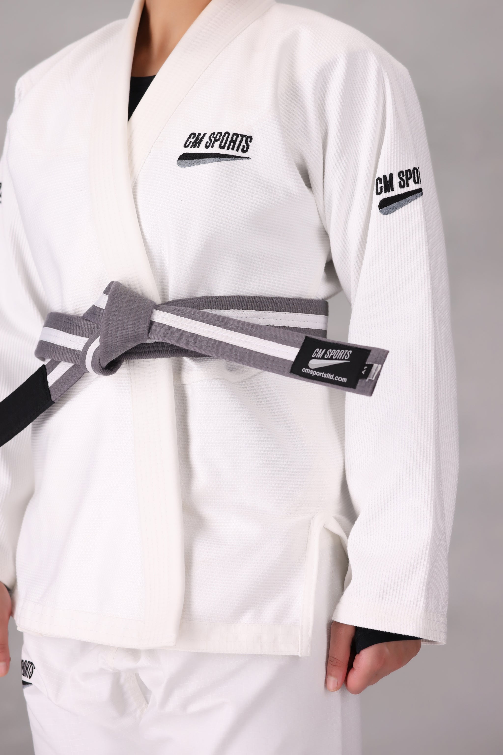Woman wearing a custom white BJJ Gi with a black belt, standing on a gray background UK Brazilian Jiu Jitsu uniform