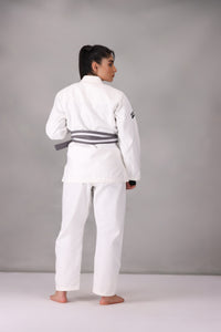 Woman wearing a custom white BJJ Gi with a black belt, standing on a gray background UK Brazilian Jiu Jitsu uniform