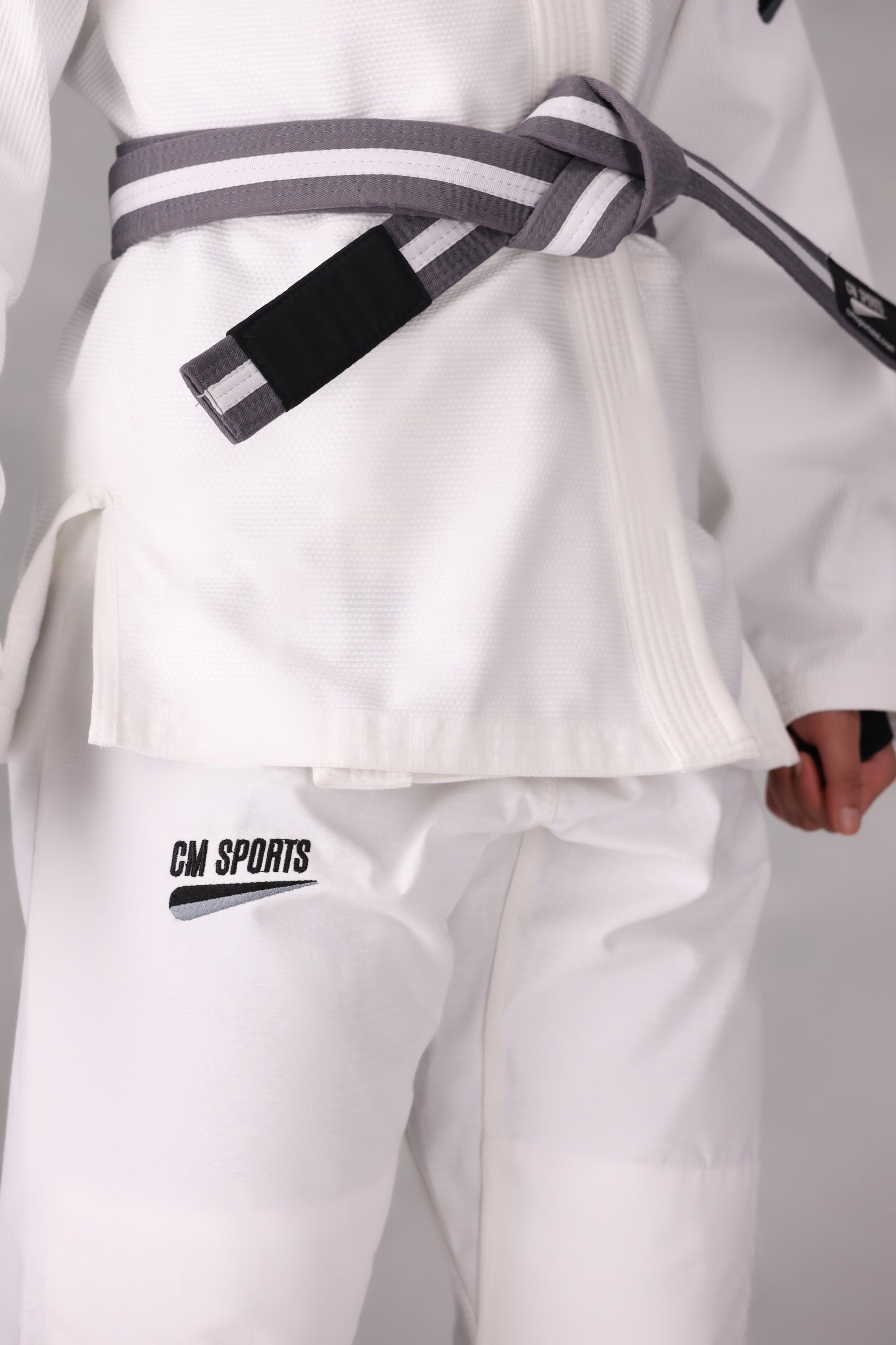 Woman wearing a custom white BJJ Gi with a black belt, standing on a gray background UK Brazilian Jiu Jitsu uniform