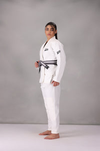 Woman wearing a custom white BJJ Gi with a black belt, standing on a gray background UK Brazilian Jiu Jitsu uniform